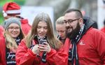 Foto: IG Metall, junge Frau tippt in Handy in einer Menschenmenge und junger Mann schaut zu